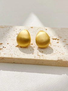 Detailed view of teardrop earrings with a golden brushed matte finish on stone stand