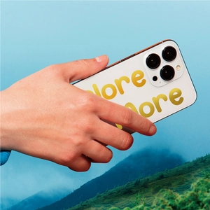Close-up of white iPhone case with gold Explore More text held against mountain landscape