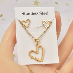 Macro detail of golden stainless steel heart and arrow necklace with matching stud earrings
