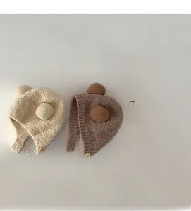 Detailed view of knitted baby earflap hats with pom-poms and wooden buttons in beige and brown