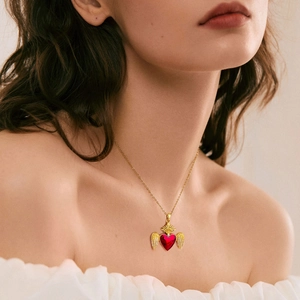 Close-up of a gold-plated necklace with a ruby red heart pendant and angel wings detail
