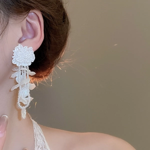 Detail of white 3D floral drop earrings with elegant beaded tassels on a model