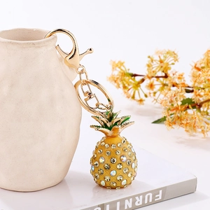 Detailed view of rhinestone pineapple keychain with golden lobster clasp on a white vase