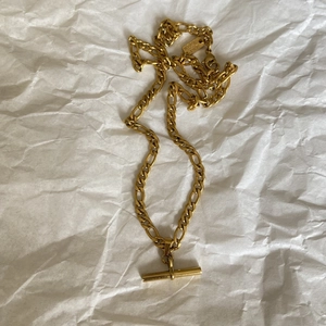 Detail of 18K gold-plated T-bar pendant necklace featuring a polished Figaro chain link