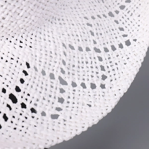 Detailed macro view of white woven straw hat featuring intricate hollow-out floral patterns
