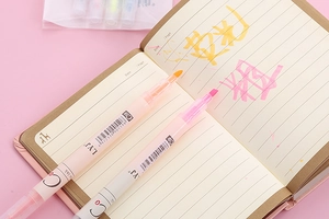 Macro shot of dual-tip highlighter pen nibs creating bright marks on notebook paper