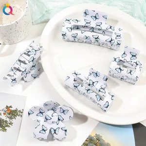 Flat lay of five assorted white acrylic hair claws with blue butterfly prints in a ceramic tray