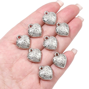 Detailed view of silver heart-shaped pendants with floral relief held in palm