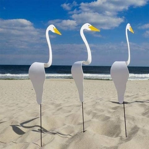 Three elegant white Swirl Bird wind spinners standing on a beach against blue sea and sky