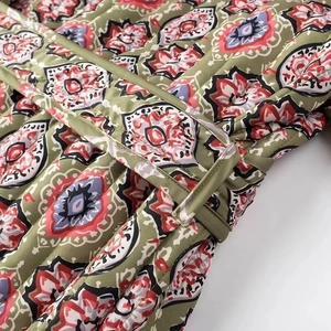 Detail of olive green quilted jacket with floral patterns and matching waist belt