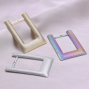 Detailed close-up of square metal earrings in gold, silver, and rainbow with dotted texture