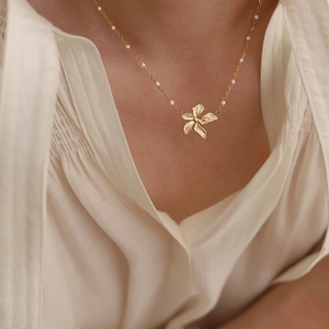 Detail of 18K gold flower pendant necklace with white beads on a soft beige shirt
