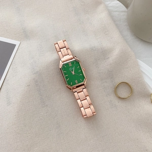Detail of rose gold rectangular watch with green dial on elegant linen background