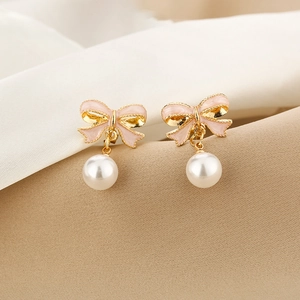 Macro shot of elegant pink bow earrings with white pearl pendants on satin background