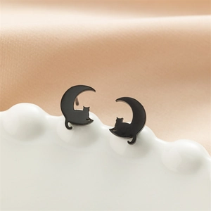 Detailed close-up of black cat and moon stainless steel stud earrings on ceramic tray