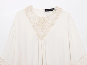 Close-up of white long sleeve blouse featuring intricate lace V-neck patchwork detail