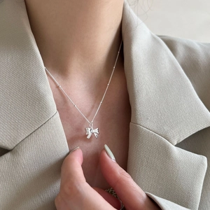 Elegant silver bow pendant necklace with beaded titanium steel chain worn by a model