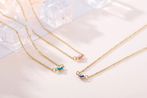 Close-up of three gold evil eye necklaces with colorful enamel pendants on pink background