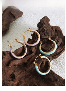 Detail of colorful enamel hoop earrings with zircons on a rustic dark wood stand