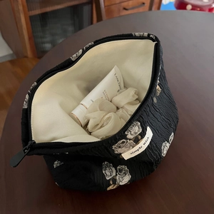 Detailed close-up of a floral jacquard makeup bag with white rose patterns on wood table