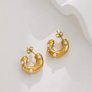 Macro shot of 18k gold C-shaped earrings with pearls and crystals on white background
