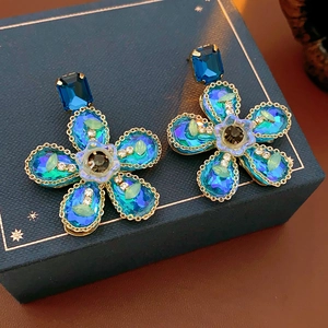 Détail de boucles d'oreilles fleur avec cristaux bleus et verts sur un écrin