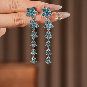 Détail de boucles d'oreilles fleur à pompons bleus portées par un mannequin chic