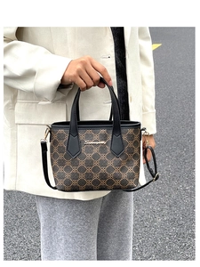 Detailaufnahme der braunen Monogramm-Handtasche mit goldenem Logo und schwarzen Griffen