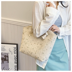 Détail d'un sac cabas en paille beige avec broderie florale et poignées en corde torsadée