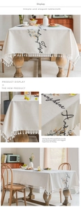 Detail of embroidered leaves and cursive letters on beige tablecloth with elegant fringe trim