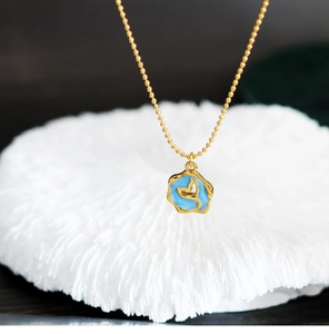 Macro view of gold beaded chain necklace with blue enamel fishtail pendant on coral