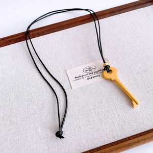 Close-up of a vintage golden key pendant with black leather cord on a linen tray