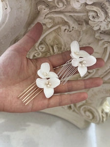 Close-up of small white ceramic flower hair combs with freshwater pearls in hand