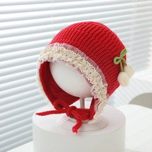 Detail of red knit baby hat with white lace trim, green bow and cute fuzzy pompom
