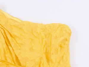 Close-up of yellow pleated fabric with textured jacquard pattern for French style dress