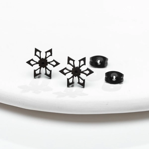 Macro detail of black snowflake stud earrings with butterfly backs on white surface