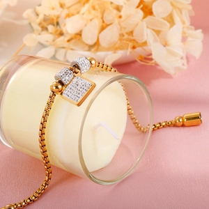 Détail d'un bracelet en titane doré avec breloques en cristal sur un bougeoir blanc