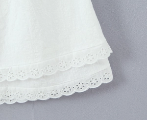 Close-up of white dress hem featuring delicate eyelet embroidery and scalloped lace edges