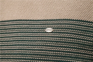 Detailed close-up of knit fabric texture with beige and dark green stripes and logo plate