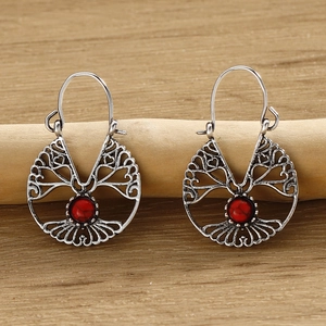 Detailed view of silver tree of life earrings with red round stone on wood background