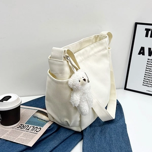 White canvas crossbody bag with plush bear pendant on denim fabric background