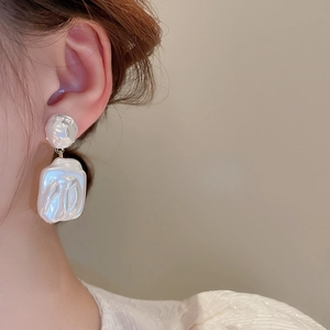 Primo piano di orecchini di perla barocca con pendente rettangolare bianco su modella