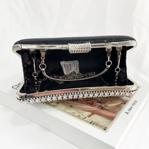 Elegant black evening clutch with rhinestone trim and metal chain strap on white fabric