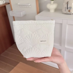 Detail of white quilted shell cosmetic bag with textured scallop stitching and zipper