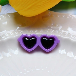 Miniature purple heart sunglasses accessory displayed on a white textured ceramic dish