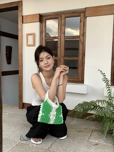 Detail of green and white crochet handbag with geometric patterns held by a model
