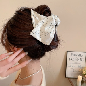 Detail shot of a white fabric hair bow with blue polka dots worn on a hair bun