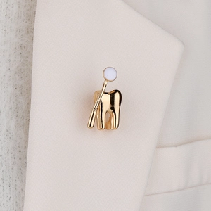 Broche créative en forme de dent plaquée or sur le revers d'un tailleur blanc