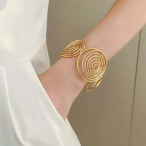 Close-up of golden spiral wave bangle showing metallic texture and modern geometric style
