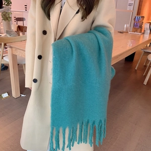 Close-up of soft turquoise mohair scarf with tassels held by a model in a cafe